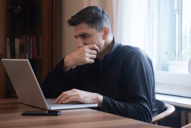 homem com expressão de preocupação olhando um boleto falso na tela do computador