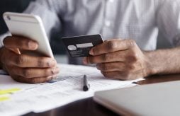Homem pagando IPVA na internet usando cartão de crédito e telefone celular