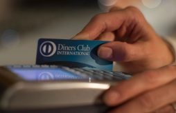mão passando um cartão de crédito Diners Club em uma maquininha de cartão