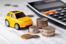 Carro e moedas com calculadora simulando um empréstimo com garantia de veículo