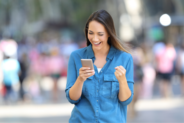 Uma mulher com expressão de felicidade segurando um celular em uma das mãos