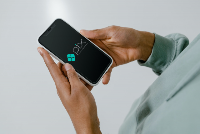Imagem de uma pessoa segurando um smartphone nas mãos onde se vê na tela o logotipo do Pix do Banco Central