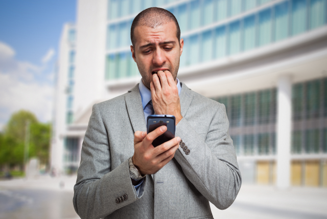Um homem de terno segurando um celular e levando uma mão a boca com expressão de preocupação por não saber como fazer estorno de pix