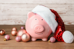 um cofre em forma de porquinho usando um gorro de natal ao lado de enfeites natalinos para exemplificar como fazer dinheiro no natal