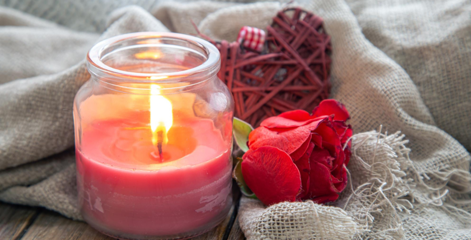 uma vela aromática acesa dentro de um pote de vidro ao lado de uma rosa