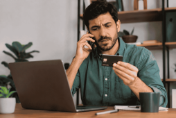 um homem falando ao celular e segurando um cartão para ilustrar Como fazer o estorno de débito