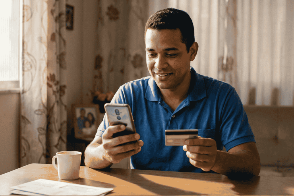 um homem usando o celular e segurando um cartão de débito para ilustrar se Empregado pode fechar conta salário