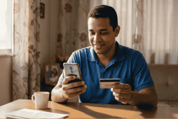um homem usando o celular e segurando um cartão de débito para ilustrar se Empregado pode fechar conta salário