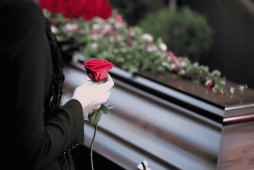 mulher segurando uma rosa em frente a uma urna funerária para ilustrar conta bancária de falecido