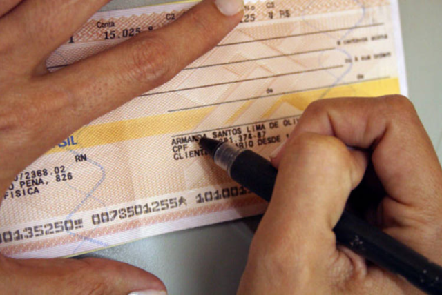 mão preenchendo talão - Diferença entre talão de cheque e cheque especial