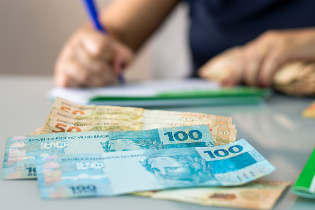 uma pessoa assinando o contrato de um empréstimo para assalariado e alguma notas de dinheiro sobre a mesa