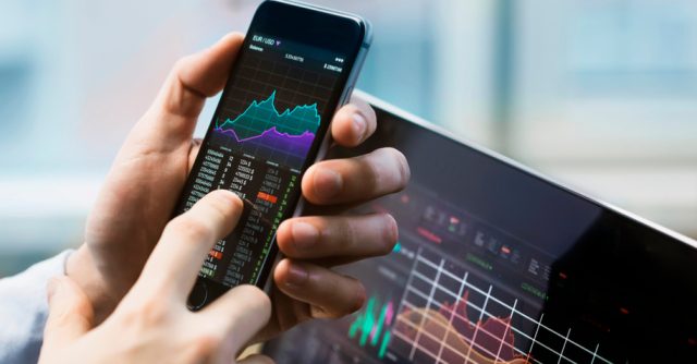 Homem segurando um celular com gráficos- Rico Investimentos é uma boa corretora? Avaliação completa!