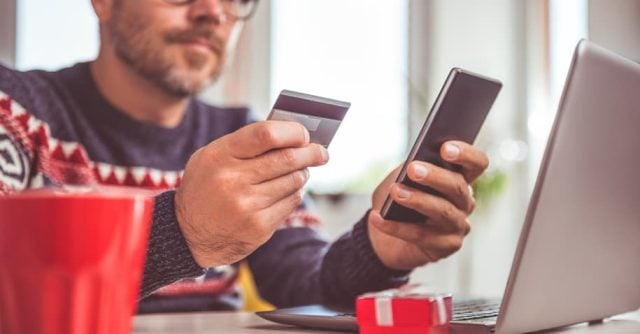 Homem segurando cartão de crédito em uma mão e o celular em outra- Como tirar a 2ª via da fatura hipercard: um guia simples e prático
