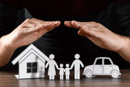 uma pessoa com as mãos sobre figuras de uma casa, carro e família exemplificando Seguro e prevenção de dívidas