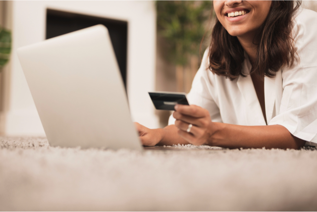 mulher segurando um cartão enquanto usa um notebook para ilustrar o tema cartão para compras online