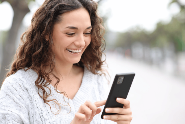 mulher sorrindo usando o celular para tirar a cemig segunda via