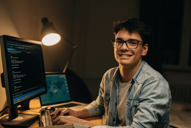 Jovem freelancer sorrindo enquanto trabalha em um projeto no computador, ilustrando como ganhar dinheiro na Fiverr