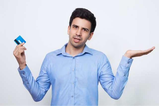 homem segurando um cartão de crédito com uma mão e a outra em posição de dúvida sobre como funciona o cartão de crédito