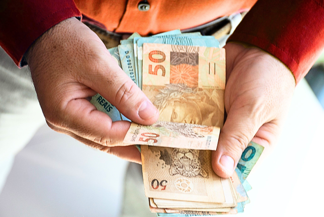 mãos segurando notas de dinheiro - salário mínimo 2025