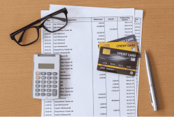 óculos, planilha, calculadora e cartões sobre uma mesa para representar como dividir fatura do cartão