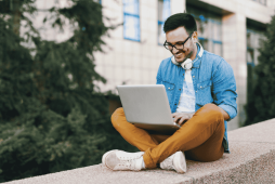 rapaz sentando ao ar livre usando computador para trabalhos freelancers